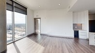 Located on the 17th floor of Brooklyn Village in uptown Charlotte, this contemporary residence offers three bedrooms, four bathrooms, and a thoughtfully designed open-concept layout. The living room is a showstopper, featuring floor-to-ceiling windows that frame dramatic panoramic views of the Charlotte skyline, bathing the space in abundant natural light. Light-toned hardwood-style flooring flows throughout the main living areas, complementing the clean, modern aesthetic.

The sleek kitchen is outfitted with white flat-panel cabinetry, stainless steel appliances, a substantial stone-topped island with pendant lighting above, and expansive windows that continue the stunning city views. The open design allows for seamless flow between cooking and entertaining areas.

The generously sized primary bedroom features soft carpeting, a tray ceiling detail, and direct access to a well-appointed en-suite bathroom with dark granite countertops, a framed mirror, and a glass-enclosed tiled shower. Two walk-in closets provide ample built-in shelving and hanging space for organized storage. The additional bedrooms are bright and carpeted, each with access to their own bathrooms. Throughout, the residence maintains a refined, neutral palette with modern hardware and finishes that reflect sophisticated urban living.