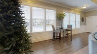 This well-appointed single-floor space is designed for comfort and functionality, offering a generous open layout that flows seamlessly between multiple distinct areas. The expansive main living area features a tray ceiling with crown molding, plush carpeting, and a stone-surround fireplace flanked by built-in shelving and cabinetry — an ideal focal point for the room. A wall-mounted television above the fireplace adds a modern touch, while arched doorway details lend architectural character throughout.

Multiple seating arrangements accommodate both intimate gatherings and larger groups, including leather lounge chairs and a curved sectional sofa centered on a decorative area rug. Large windows fitted with wood blinds line the perimeter, flooding the interior with natural light and offering outdoor views of the surrounding neighborhood.

A bright dining nook with high-top seating sits adjacent to the main area, benefiting from an expansive bank of windows. The kitchen is well-equipped with white shaker cabinetry, light quartz countertops, stainless steel appliances including a refrigerator and oven, a double-basin sink, and wood-look flooring. A secondary kitchenette area provides additional prep and storage space. The overall aesthetic is cohesive and polished, with neutral tones accented by teal cabinetry pieces.