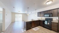 Located at 4918 S Center St in Murray, Utah, this well-appointed one-bedroom, one-bathroom unit offers a thoughtfully designed single-floor layout. The open-concept living and kitchen area is anchored by a peninsula-style kitchen featuring dark espresso cabinetry, granite countertops, a built-in sink, black appliances, and stylish pendant lighting that illuminates the space. Light wood-style flooring runs throughout the main living area, creating a clean, cohesive look, while a sliding glass door floods the living room with natural light and provides outdoor access. The bedroom is generously sized with plush wall-to-wall carpeting, a window with blinds, and direct access to a dedicated walk-in closet, offering ample storage. The full bathroom continues the upscale finishes with dark wood cabinetry, granite countertops, a large vanity mirror with overhead lighting, and a full tub-shower combination with tile flooring. A separate laundry room with a full-size washer and dryer and additional shelving adds everyday convenience. The unit's neutral color palette and consistent finishes throughout create a comfortable, functional living environment suited for modern everyday life.