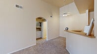 This single-story home is designed with a bright, open layout that maximizes the sense of space throughout. The living area is a standout feature, boasting soaring vaulted ceilings and a ceiling fan overhead. Soft carpeting covers the floor, and a large window dressed with vertical blinds allows natural light to fill the room, creating a welcoming ambiance. A tiled entryway provides a clean transition into the carpeted living space, and an elegant arched doorway adds an architectural detail that connects the main living area to the rest of the home.

The kitchen is well-equipped with ample white cabinetry, warm-toned countertops, and tile flooring. It includes a full suite of white appliances — a coil-top range with an over-the-range microwave, and a dishwasher — along with generous counter space for meal preparation. A dedicated laundry room is conveniently located within the home, housing a full-size top-load washer and dryer alongside a water heater, with shelving for additional storage.

The bathroom features a tub-shower combination with tiled surround, a toilet, and a vanity with white cabinetry and a warm-toned countertop, all set on tile flooring. The home's neutral color palette, vaulted ceilings, and functional layout come together to create a comfortable and practical living environment.