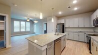 This single-story residence is designed with a contemporary, open-concept layout that connects the kitchen and living areas seamlessly. The kitchen serves as the centerpiece of the space, showcasing a large granite-topped island with an integrated sink and pendant lighting overhead. White shaker-style cabinetry lines the walls, complemented by granite countertops and a full suite of stainless steel appliances, including a refrigerator, electric range, built-in microwave, and dishwasher. Light wood-look flooring runs throughout the main living areas, contributing to a bright, cohesive aesthetic.

The living area extends naturally from the kitchen, featuring a ceiling fan, recessed lighting, and a window that allows natural light to fill the space. Multiple bedrooms offer plush carpeting, ceiling fans, and windows with blinds. At least one bedroom includes access to a dedicated walk-in closet with built-in shelving for organized storage.

The bathrooms are finished with granite-topped vanities, gray cabinetry, and tile-surround tub and shower combinations. Light wood-look flooring carries through these spaces, maintaining a consistent, clean design throughout the unit.