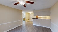 This thoughtfully laid-out 1-bedroom, 1-bathroom unit offers a practical and comfortable living experience across a single floor. The open-concept kitchen and living room form the heart of the space, featuring light wood-style vinyl flooring, warm beige walls, and a textured ceiling throughout. A ceiling fan with a light fixture provides both air circulation and ambient lighting in the living area, which also includes a chair-rail detail along the walls for a classic touch.

The kitchen is defined by a peninsula-style breakfast bar with a dark granite-look countertop, warm wood cabinetry, a double-basin sink, and white appliances including a refrigerator, stove, and dishwasher. The living area opens directly to a private balcony through a sliding glass door, allowing natural light to filter in.

The bedroom is generously sized with plush carpet flooring, a ceiling fan, a window with blinds, and a mirrored sliding-door closet that adds a sense of depth and storage practicality. A hallway connects the main living spaces to the bedroom and bathroom.

The bathroom is clean and functional, featuring a tub-shower combination with tile surround, a wood vanity with a dark countertop, a large mirror, and vinyl flooring consistent with the rest of the unit.