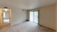 This single-floor unit offers a practical and straightforward layout across two bedrooms and one bathroom. The living room serves as the central gathering space, featuring neutral-toned wall-to-wall carpeting, a textured ceiling, and a full-width sliding glass door dressed with vertical blinds. The door provides direct access to an outdoor area and allows natural light and views of surrounding greenery to filter into the room.

Both bedrooms continue the carpeted flooring and textured ceiling aesthetic, each featuring a window with blinds that admit natural light while maintaining privacy. The rooms offer clean, neutral walls providing a versatile backdrop for various furnishing arrangements.

The kitchen is efficiently designed with light wood cabinetry above and below the countertops, a white refrigerator, and a sink along the perimeter. The layout maximizes the available space while keeping a clean, functional appearance.

The bathroom includes a full-size soaking tub with an overhead shower, a toilet, and a textured ceiling consistent with the rest of the unit. The fixtures are finished in white with chrome hardware, contributing to a clean and utilitarian aesthetic throughout the space.