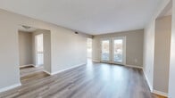 This single-floor, 2-bedroom, 2-bathroom home offers a clean, modern aesthetic with a neutral color palette and hardwood-style flooring that flows consistently throughout every room. The living room is a bright, open space anchored by a set of French doors that flood the area with natural light and provide outdoor access, creating an airy and welcoming atmosphere. A ceiling fan adds functionality to the adjoining area, which connects seamlessly to the rest of the layout via hallways.

The galley-style kitchen is efficiently designed with white shaker cabinetry lining both walls, granite-look countertops, a double-basin sink, and white appliances including a range and refrigerator. Natural light enters through a window at the far end, making the kitchen feel bright and practical.

Both bedrooms feature the same hardwood-style flooring, neutral warm-toned walls, and windows with blinds that allow for natural light and privacy. The primary bedroom offers a comfortable footprint with dedicated closet access.

The two bathrooms are identically outfitted with white vanity cabinetry, granite-top sinks, brushed nickel fixtures, backlit mirrors, and clean tile-free hardwood-style floors. One bathroom includes a bathtub. The home also includes a utility room and dedicated closet space, rounding out a highly functional and cohesive floor plan.