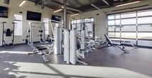 This 1,460-square-foot fitness center in Salt Lake City, Utah, offers a comprehensive workout experience within a single-floor layout. The space is characterized by its modern industrial design, featuring high ceilings with exposed ductwork and contemporary lighting fixtures. Large windows flood the area with natural light, creating an energizing atmosphere.

The facility is divided into distinct zones for various exercise types. A cardio area is equipped with state-of-the-art treadmills, ellipticals, and stationary bikes, all positioned to take advantage of the outdoor views. The strength training section includes a range of weight machines and free weights, with ample space for lifting and functional exercises.

A dedicated area for stretching and bodyweight exercises is evident, complete with mats and stability balls. The center also incorporates a separate room for group classes or personal training sessions, outfitted with additional equipment like squat racks and bench press stations.

Convenience is key, with a locker area providing secure storage for personal belongings. The overall design emphasizes cleanliness and functionality, with durable flooring and strategically placed mirrors to assist with form during workouts. Multiple wall-mounted TVs offer entertainment options, while the open floor plan promotes a sense of spaciousness and community among gym-goers.