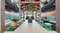 Located at 6650 Liberty Grand Blvd. in Powell, Ohio, this single-story clubhouse is a masterclass in biophilic design and vibrant interior styling. The grand entrance greets visitors with soaring cathedral ceilings supported by exposed wooden beams and timber columns, paired with light herringbone-patterned flooring that sets an elegant tone. Floor-to-ceiling windows flood the space with natural light and provide views of the surrounding landscape.

The expansive main hall features living birch trees planted in oversized planters, creating an immersive indoor-garden atmosphere. Teal upholstered banquette seating with herringbone wood accent walls lines one side, while curated lounge areas offer lush green velvet sofas, gold-accented tables, and mixed seating arrangements throughout.

A cozy lounge zone features a dramatic suspended fireplace encircled by colorful velvet ottomans and plush seating, adjacent to a café with a teal service counter. Nearby, a bold tropical floral wallpaper accent wall anchors a vibrant sitting area with a deep burgundy rug.

A private dining nook showcases a live-edge wood table beneath a statement crane mural and a sculptural ring chandelier. The space also includes a full media lounge with a marble-topped bar, mounted TVs, and pendant lighting. Wide, well-lit corridors connect additional rooms throughout this thoughtfully designed facility.