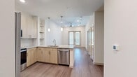 Located at 125 S Standridge Blvd in Anna, TX, this thoughtfully designed one-bedroom, one-bathroom unit offers a efficient and modern living experience across a single floor. The open-concept layout seamlessly connects the kitchen and living room, creating a bright and airy atmosphere enhanced by recessed lighting and a ceiling fan overhead.

The kitchen is a standout feature, showcasing light wood cabinetry, granite countertops, a peninsula with pendant lighting, and a full suite of stainless steel appliances including a refrigerator, range, microwave, and dishwasher. Open shelving adds both functionality and a contemporary aesthetic touch.

The living room is bathed in natural light through stylish French doors that open to the outside, with wood-look flooring flowing throughout the main living areas. The bedroom offers plush carpeting, tall windows that invite ample daylight, and soaring ceilings that lend a sense of generous vertical space.

The bathroom features a granite-topped vanity with light wood cabinetry and wood-look flooring. Directly accessible from the bathroom is a well-organized walk-in closet complete with built-in shelving and a hanging rod, providing excellent storage. Clean white walls and neutral finishes throughout give the space a fresh, modern ambiance.