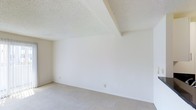 This single-floor space presents a clean, minimalist interior designed with simplicity and functionality in mind. The room showcased features smooth, white-painted walls that reflect light evenly throughout the space, contributing to a bright and airy atmosphere. Underfoot, a neutral-toned carpet provides a soft, comfortable surface that complements the overall light color palette.

A notable architectural detail is the angled ceiling soffit, which adds a subtle geometric element to the room's upper portion. The textured popcorn ceiling finish is consistent throughout, adding a classic residential character to the space. Electrical outlets are positioned at standard intervals along the baseboards, offering practical utility placement.

The room's neutral tones — whites, creams, and beiges — create a versatile blank canvas well-suited for a variety of furniture arrangements and décor styles. The absence of furnishings allows the structural features to stand out, highlighting the room's generous proportions and clean lines. Overall, the space offers a straightforward, functional layout with a light, open ambiance ready for personalization.
