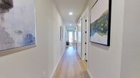 This single-floor residence presents a thoughtfully designed layout with a clean, contemporary aesthetic carried consistently throughout. Light hardwood flooring runs through the main living areas, connecting each space with a warm, cohesive tone.

The open-concept kitchen and living area form the heart of the unit. The kitchen is outfitted with dark espresso cabinetry, light quartz countertops, a subway tile backsplash, and a full suite of stainless steel appliances, including a refrigerator, dishwasher, microwave, and range. A deep undermount sink with a matte black faucet adds a refined touch. Natural light enters through a large window, brightening the space.

The living area accommodates comfortable seating and a large flat-screen television, with a ceiling fan overhead and access toward the hallway. A long, well-lit corridor connects the living spaces to the private quarters, featuring framed artwork along neutral walls.

The bedroom is a restful retreat with a padded upholstered headboard, ceiling fan, and direct access to the en-suite bathroom. The bathroom features dark wood cabinetry, a single undermount sink with gray countertop, a framed mirror, and large-format dark tile flooring. A spacious walk-in closet with wrap-around shelving and hanging rods provides generous storage.