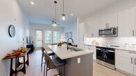 Located in Palm Harbor, Florida, this well-appointed one-bedroom, one-bathroom residence offers a thoughtfully designed open-concept layout. Light-toned luxury vinyl plank flooring flows throughout, complementing the bright, neutral color palette that defines the space.

The combined kitchen and living area serves as the heart of the home. The kitchen is outfitted with crisp white shaker cabinetry, stainless steel appliances including a refrigerator, range, and microwave, and a large central island with a quartz countertop, undermount sink with a matte black faucet, and bar seating for multiple guests. Globe pendant lights add a stylish finishing touch overhead. The living area benefits from an abundance of natural light through large windows with plantation-style blinds and direct access to a private balcony.

The bedroom is a serene retreat featuring clean lines, light wood flooring, and ample space for furnishings. Two closets provide generous storage throughout the unit. The bathroom includes a tub-shower combination with tiled surround, matte black fixtures, and a warm wood-toned vanity with a light countertop. An in-unit laundry area adds everyday convenience to this modern, move-in-ready home.