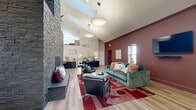 Located at 2400 Village Rd in Pittsburgh, PA, this single-floor community clubhouse offers an expansive and thoughtfully designed gathering space. The centerpiece of the main lounge is a striking floor-to-ceiling stacked stone fireplace that anchors the open-concept layout beneath soaring vaulted ceilings with skylights, flooding the space with natural light. Light wood flooring runs throughout, complementing the airy, contemporary aesthetic. The lounge area is furnished with comfortable seating, a wall-mounted television, and a dining arrangement, making it ideal for socializing and relaxation. A bold, wine-red accent wall adds warmth and character to the seating zone. The kitchen area features a large white marble-topped island with bar seating and a teal mosaic tile backsplash, alongside stainless steel appliances. The expansive fitness center is exceptionally well-equipped, boasting treadmills, ellipticals, cable machines, rowing equipment, and mirrored walls beneath high ceilings with skylights that keep the workout environment bright and energizing. A dedicated tanning room with warm-toned walls and a full-length mirror rounds out the amenities. Ceiling fans, recessed lighting, and an abundance of windows ensure comfort and brightness throughout this versatile community space.