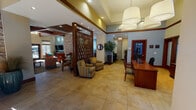 Located in Maple Valley, Washington, this single-story community clubhouse at 22435 SE 240th St offers a thoughtfully designed gathering space with a blend of warm, contemporary finishes throughout. The welcoming lobby greets visitors with large-format tile flooring, soaring ceilings, and an elegant front desk crafted from rich wood tones. A distinctive diamond-patterned wood screen partition divides the entry from adjoining lounge areas, adding architectural interest and visual depth.

The main lounge features dramatic exposed wood beam ceilings, floor-to-ceiling stacked stone accent walls, and abundant natural light streaming through tall windows. Comfortable seating arrangements invite relaxation, complemented by warm neutral tones and curated décor. A secondary lounge area with a wall-mounted flat-screen TV and built-in wood shelving opens directly to the outdoor pool area via glass doors, seamlessly connecting indoor and outdoor living.

The well-appointed kitchen includes rich wood cabinetry, granite countertops, stainless steel appliances, a tile backsplash, and a central island with bar seating — ideal for community gatherings and events. A dedicated prep kitchen with additional cabinetry, granite surfaces, and a garden window overlooking lush greenery provides supplementary functionality. Together, these spaces create a cohesive, inviting environment suited for a variety of community activities.