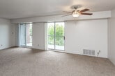 This single-floor residence offers a thoughtfully arranged layout that balances open living spaces with functional private rooms. The expansive main living area is a standout feature, highlighted by two sliding glass doors that open onto a balcony, filling the room with abundant natural light and providing views of the surrounding greenery. A ceiling fan with a light fixture anchors the space, while wall-to-wall carpeting and a textured ceiling contribute to a warm, comfortable atmosphere.

The kitchen is efficiently designed with white cabinetry extending to the ceiling, ample counter space, and a full suite of appliances including a refrigerator, electric range, and dishwasher. Light tile flooring completes the practical workspace.

The bedrooms are generously proportioned, each featuring soft carpeting, neutral walls, and large windows dressed with vertical blinds that offer both natural light and privacy. The primary bedroom includes an en-suite bathroom, while a second bedroom features a closet. Additional carpeted rooms provide flexible space throughout.

The bathroom is fitted with a vanity featuring a marble-patterned countertop, white cabinetry, and a tiled shower and floor, offering a clean and functional design.