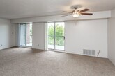 This single-floor residence offers a thoughtfully arranged layout that balances open living spaces with functional private rooms. The expansive main living area is a standout feature, highlighted by two sliding glass doors that open onto a balcony, filling the room with abundant natural light and providing views of the surrounding greenery. A ceiling fan with a light fixture anchors the space, while wall-to-wall carpeting and a textured ceiling contribute to a warm, comfortable atmosphere.

The kitchen is efficiently designed with white cabinetry extending to the ceiling, ample counter space, and a full suite of appliances including a refrigerator, electric range, and dishwasher. Light tile flooring completes the practical workspace.

The bedrooms are generously proportioned, each featuring soft carpeting, neutral walls, and large windows dressed with vertical blinds that offer both natural light and privacy. The primary bedroom includes an en-suite bathroom, while a second bedroom features a closet. Additional carpeted rooms provide flexible space throughout.

The bathroom is fitted with a vanity featuring a marble-patterned countertop, white cabinetry, and a tiled shower and floor, offering a clean and functional design.