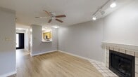 This classic two-story home offers three bedrooms and one bathroom thoughtfully distributed across two floors. The main level opens into a bright living room featuring light wood-look flooring, a ceiling fan with track lighting, and a tile-surround fireplace as a focal point. French doors flood the space with natural light and provide outdoor access. A pass-through window connects the living area to the kitchen, which is equipped with warm wood cabinetry, white countertops, a stainless steel range, built-in microwave, dishwasher, and a double sink — all set on matching light wood flooring. A staircase with a wood handrail leads to the upper floor, where the three bedrooms are located. The generously sized primary bedroom features vaulted ceilings, a ceiling fan, and a walk-in closet. The additional bedrooms are well-proportioned, each with ceiling fans and natural light from windows with blinds. The full bathroom includes a tiled tub-shower combination with chrome fixtures. A dedicated laundry area with washer hookups, built-in shelving, and a window completes the upper level. Neutral gray walls and consistent light wood flooring throughout give the home a clean, cohesive aesthetic.