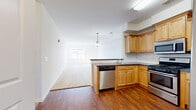 Located at 101 Prosper Way in Brick, NJ, this one-bedroom, one-bathroom residence offers a well-organized single-floor layout designed for comfortable everyday living. The open-concept kitchen flows seamlessly into the living area, creating a connected and functional common space. The kitchen is equipped with warm honey-toned wood cabinetry, dark countertops, a white subway tile backsplash, and a full suite of stainless steel appliances including a gas range, over-the-range microwave, dishwasher, and a side-by-side refrigerator with ice and water dispenser. Rich hardwood-style flooring anchors the kitchen and entry hallway, adding warmth and durability. The living room features plush neutral carpeting and a large window that draws in natural light. The spacious bedroom continues the carpet flooring and is brightened by a window with views of the surrounding community, complemented by a dedicated closet for ample storage. The bathroom is finished with matching wood-toned cabinetry, a mirrored medicine cabinet, a combination tub and shower, and hardwood-style flooring, with accessibility-friendly grab bars incorporated throughout. Clean white walls and consistent finishes throughout give the space a bright, move-in-ready feel.