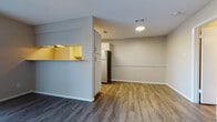 This single-story residence is designed with a practical, open-concept layout that connects the living area and kitchen seamlessly. The living space features wood-look laminate flooring in a warm honey tone, neutral-colored walls, and a sliding glass door fitted with vertical blinds that allows natural light to fill the room. A second area with darker wood-look flooring is also present, adding visual contrast throughout the unit.

The kitchen is partially separated by a half-wall partition that creates a pass-through opening, providing sightlines between the kitchen and living areas. White cabinetry lines the kitchen walls, complemented by a stainless steel refrigerator and additional appliances. A dedicated in-unit laundry area is accessible directly from the kitchen, housing a washer and dryer and offering added everyday convenience.

The bedrooms are carpeted in a neutral beige tone and each feature ceiling fans with light fixtures, windows that bring in natural light, and ample wall space. Doors lead to what appear to be closets, providing functional storage. The overall ambiance of the residence is clean, bright, and move-in ready, with a straightforward layout that makes efficient use of the available space.