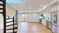 Located in Washington, DC's vibrant Capitol Hill neighborhood, Unit 403 at 716 L St SE is a thoughtfully designed contemporary residence that blends modern aesthetics with functional living. The open-concept main living area is anchored by light-toned hardwood flooring that flows seamlessly throughout the space, while recessed lighting illuminates the clean white walls and crisp millwork. A striking black metal spiral staircase serves as a dramatic focal point, ascending through a skylight opening that draws natural light into the heart of the home. The living area opens to the outdoors through a set of French doors flanked by a side window, offering views of the surrounding greenery. The kitchen is outfitted with flat-front cabinetry in a warm off-white finish, a herringbone tile backsplash, white quartz countertops, and a full suite of stainless steel appliances including a gas range, built-in microwave, dishwasher, and refrigerator. A louvered pantry door adds a refined, functional detail near the kitchen entry arch. The bathroom presents a spa-like atmosphere with large-format tile flooring, a rich walnut vanity with gold hardware, matte black fixtures, and a frameless glass-enclosed walk-in shower with full-height tile surround.