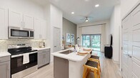 Located at 1617 Enid St in Houston, TX, this thoughtfully designed one-bedroom, one-bathroom residence offers an efficient and stylish single-floor layout. The open-concept kitchen is a standout feature, showcasing two-tone gray and white shaker cabinetry, stainless steel appliances, a decorative tile backsplash, and a central island with a built-in sink and bar seating — ideal for casual dining and entertaining. Light wood-look flooring flows throughout the main living areas, complementing the bright, neutral color palette and recessed lighting overhead. The living room is anchored by a large sliding glass door that invites natural light and opens directly onto a private patio with outdoor views. The bedroom offers plush carpeting, multiple windows, and tall ceilings that lend an airy feel, while two closets — including a spacious walk-in — provide generous storage. The full bathroom features large-format tile surrounding a soaking tub and shower combination, a dark-toned vanity with a lighted mirror, and wood-look flooring. A dedicated laundry area and hallway storage round out this well-appointed home, delivering functional comfort with modern design sensibility.