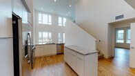 This two-story residence in Milpitas, California offers a clean, contemporary design defined by a bright, open layout and high-quality finishes throughout. The main level is anchored by a dramatic double-height living and kitchen area, where floor-to-ceiling windows flood the space with natural light and frame views of the surrounding cityscape. The kitchen is well-appointed with white cabinetry, granite countertops with a subway tile backsplash, and a full suite of stainless steel appliances including a gas range, over-the-range microwave, dishwasher, and side-by-side refrigerator. A staircase with a clean white railing leads to the upper level, where a carpeted loft-style landing overlooks the main living area through a series of windows that capture expansive outdoor views. The bedrooms are generously proportioned, finished with light hardwood flooring and bright windows that bring in natural light. The bathrooms maintain the home's modern aesthetic, featuring white vanities with dual sinks and large mirrors, as well as a glass-enclosed walk-in shower. Light hardwood flooring runs consistently throughout the main living areas, complementing the home's crisp, neutral color palette and contributing to its cohesive, contemporary feel.