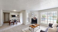 This two-bedroom, two-bathroom single-floor residence in Dallas, Texas offers a well-organized layout designed for comfortable everyday living. The living room serves as the heart of the home, featuring a classic white-mantled fireplace, soft carpeted flooring, and multiple windows that invite generous natural light and views of the outdoor pool area. The open flow connects seamlessly to the dining area, which is anchored by a sliding glass door providing additional outdoor views and easy access to the exterior. The adjacent kitchen features granite-style countertops, white cabinetry, and black appliances, with a pass-through opening that maintains visual connectivity to the dining space. Both bathrooms are finished with granite-style vanity countertops and white cabinetry; one includes a tub/shower combination with wood-look flooring. The bedrooms offer carpeted floors and ample natural light, with the primary bedroom featuring a ceiling fan and a spacious walk-in closet equipped with wire shelving on multiple walls for generous storage. A second closet provides additional storage convenience. The home's neutral color palette and textured ceilings throughout contribute to a clean, functional aesthetic suitable for a wide range of lifestyles.