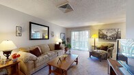 This single-floor residence offers a thoughtfully arranged layout with a seamless flow between its primary living spaces. The living room is warm and inviting, featuring plush carpeting, a large wall mirror, and sliding glass doors that open to an outdoor balcony, filling the room with natural light and providing pleasant exterior views. A second sitting area adjacent to the living room offers additional lounge space with open sightlines toward the balcony.

The dining area is conveniently positioned between the kitchen and living room, featuring light tile flooring, a ceiling fan, and window blinds that allow for controlled natural light. A wooden dining set and a classic china cabinet complete the space.

The kitchen is equipped with warm oak cabinetry, granite-style countertops, tile flooring, and a full suite of white appliances including a range, dishwasher, and refrigerator. A large window brightens the workspace naturally.

The primary bedroom is a calm retreat with soft carpeting, a ceiling fan, sage-toned walls, and curated wall art. A second bedroom, ideal as a children's room or guest space, features neutral tones and carpeted floors.

The bathroom is finished with gray tile surrounding the tub-shower combo, a wooden vanity with a white countertop, and coordinating green accents, offering a clean, functional design.