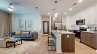 This well-designed single-floor residence showcases a thoughtful open-concept layout with modern finishes and a cohesive neutral palette throughout. Light wood-look flooring flows seamlessly across the main living areas, complementing the bright, airy atmosphere created by recessed lighting and white walls.

The kitchen serves as the centerpiece of the home, featuring a large granite-topped island with bar seating and pendant lighting overhead. Two-tone cabinetry—white uppers paired with warm wood-toned lower cabinets—provides generous storage, while stainless steel appliances, including a French door refrigerator, electric range, and microwave, complete the space. A subway tile backsplash adds a refined touch.

The open living area flows naturally from the kitchen, offering a comfortable and versatile gathering space. A well-lit hallway with decorative wall-mounted frames connects the main living zone to the private areas of the home.

Two bedrooms offer plush carpeted flooring and large windows that invite natural light. Each room is generously sized with ample space for furnishings.

The bathrooms are finished with granite-topped vanities, warm wood cabinetry, and light wood-look flooring. One bathroom features a tiled tub and shower combination, while both maintain a clean, contemporary aesthetic. Overall, this residence balances modern design with functional, comfortable living.
