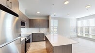 This contemporary single-floor residence showcases a thoughtfully designed open-concept layout, seamlessly connecting the kitchen, dining, and living areas. The kitchen is a standout feature, equipped with rich dark wood cabinetry, white quartz countertops, a subway tile backsplash, and a full suite of stainless steel appliances including a range, microwave, and dishwasher. A generously sized center island provides additional prep space and serves as a natural gathering point. Light hardwood-style flooring flows throughout the entire residence, complementing the neutral gray and white color palette that gives the space a clean, modern aesthetic. The living area benefits from large windows fitted with horizontal blinds, flooding the room with natural light and offering pleasant outdoor views. The bedrooms continue the bright, airy feel, each featuring large windows and built-in closets for ample storage. The bathroom is finished with large-format tile flooring, a dark wood vanity with a white countertop, and a fully tiled walk-in shower with a sliding door. Recessed lighting throughout ensures consistent illumination across all areas. The overall ambiance is fresh, contemporary, and move-in ready.