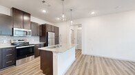 This 1-bedroom, 1-bathroom unit in Waco, TX offers a thoughtfully designed open-concept layout with modern finishes. The kitchen serves as the centerpiece of the living area, anchored by a granite-topped island with an undermount sink and stylish pendant lighting above. Rich dark espresso cabinetry extends to the ceiling, providing ample storage, while a subway tile backsplash and a full suite of stainless steel appliances — including a refrigerator, range, and built-in microwave — complete the space. Light wood-style flooring runs throughout the main living area, enhancing the bright, airy atmosphere created by recessed lighting and crisp white walls. The bedroom offers soft carpeting underfoot, a ceiling fan, and a window with natural light filtered through blinds, creating a comfortable and restful retreat. A dedicated closet provides practical storage. The bathroom features a soaking tub and shower combination with elegant large-format marble-style tile surround, paired with wood-tone cabinetry and a granite vanity top. A hallway connects all rooms efficiently, contributing to the unit's smart and functional floor plan.