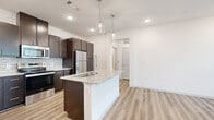 This 1-bedroom, 1-bathroom unit in Waco, TX offers a thoughtfully designed open-concept layout with modern finishes. The kitchen serves as the centerpiece of the living area, anchored by a granite-topped island with an undermount sink and stylish pendant lighting above. Rich dark espresso cabinetry extends to the ceiling, providing ample storage, while a subway tile backsplash and a full suite of stainless steel appliances — including a refrigerator, range, and built-in microwave — complete the space. Light wood-style flooring runs throughout the main living area, enhancing the bright, airy atmosphere created by recessed lighting and crisp white walls. The bedroom offers soft carpeting underfoot, a ceiling fan, and a window with natural light filtered through blinds, creating a comfortable and restful retreat. A dedicated closet provides practical storage. The bathroom features a soaking tub and shower combination with elegant large-format marble-style tile surround, paired with wood-tone cabinetry and a granite vanity top. A hallway connects all rooms efficiently, contributing to the unit's smart and functional floor plan.