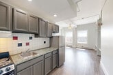Located in Worcester, MA, this efficiently designed studio presents a thoughtful single-floor layout that maximizes every square foot. The combined kitchen, dining, and living area forms the heart of the space, where gray shaker-style cabinetry, granite-look countertops, a stainless steel sink, and a full-size refrigerator define the kitchen zone. A decorative tile backsplash with colorful accent tiles adds a distinctive visual touch. The open living area flows seamlessly from the kitchen, featuring light-toned laminate hardwood flooring, a ceiling fan with integrated lighting, and exposed industrial-style track lighting that lends a modern edge. Large windows along one wall invite generous natural light and offer views of the surrounding Worcester cityscape, while a baseboard heating system ensures year-round comfort. Built-in shelving and hanging rods along one wall provide ample storage and organizational flexibility. The full bathroom is finished with warm terracotta floor tiles, classic white subway tile surrounding a full soaking tub, and bold accent tile details that echo the kitchen's design language. A dedicated utility room and a closet round out the layout, adding practical storage solutions. The overall aesthetic is clean, bright, and functional, making this a well-appointed space in the heart of Worcester.