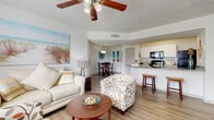 This single-floor residence exudes a relaxed, coastal charm throughout its well-designed layout. The open-concept living and dining area serves as the heart of the home, featuring warm wood-look flooring, a ceiling fan with light fixture, and a textured ceiling. Coastal-themed artwork and natural light from large windows with blinds create a bright, airy atmosphere. The living area flows seamlessly into the dining space, which is highlighted by a pendant light fixture overhead.

The galley-style kitchen is efficiently laid out with white cabinetry, dark granite countertops, and black appliances including a range, microwave, and refrigerator. A breakfast bar with seating connects the kitchen to the main living area, enhancing the open feel.

The bedrooms are comfortably sized, with the secondary bedroom featuring carpet flooring and ample natural light from dual windows. The primary bedroom is a serene retreat with neutral tones and a ceiling fan. A walk-in closet with wire shelving provides generous storage.

The bathroom is clean and functional, featuring wood-look flooring, a granite vanity with white cabinetry, and a shower-tub combination. A dedicated in-unit laundry area with a stacked washer and dryer adds everyday convenience. Throughout, the home maintains a cohesive, light-filled aesthetic.