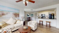This single-floor residence exudes a relaxed, coastal charm throughout its well-designed layout. The open-concept living and dining area serves as the heart of the home, featuring warm wood-look flooring, a ceiling fan with light fixture, and a textured ceiling. Coastal-themed artwork and natural light from large windows with blinds create a bright, airy atmosphere. The living area flows seamlessly into the dining space, which is highlighted by a pendant light fixture overhead.

The galley-style kitchen is efficiently laid out with white cabinetry, dark granite countertops, and black appliances including a range, microwave, and refrigerator. A breakfast bar with seating connects the kitchen to the main living area, enhancing the open feel.

The bedrooms are comfortably sized, with the secondary bedroom featuring carpet flooring and ample natural light from dual windows. The primary bedroom is a serene retreat with neutral tones and a ceiling fan. A walk-in closet with wire shelving provides generous storage.

The bathroom is clean and functional, featuring wood-look flooring, a granite vanity with white cabinetry, and a shower-tub combination. A dedicated in-unit laundry area with a stacked washer and dryer adds everyday convenience. Throughout, the home maintains a cohesive, light-filled aesthetic.
