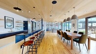 Located at 2 Chestnut St in Norwalk, Connecticut, this thoughtfully designed single-floor communal space offers a generous and versatile layout across a well-appointed open floor plan. Wide-plank natural wood flooring flows throughout, complemented by striking wood-paneled ceilings that lend warmth and a refined, contemporary character to the interior.

The living area serves as the heart of the space, anchored by a sleek concrete fireplace wall with built-in open shelving on either side. Comfortable seating — including a plush sofa and a set of leather armchairs — is arranged to encourage relaxed conversation, while a sculptural sputnik-style chandelier adds a modern focal point overhead.

Adjacent to the living area, a large dining table with ample seating sits beneath a trio of oversized dome pendant lights, making it ideal for group gatherings. A full-size pool table rounds out the recreational offerings, positioned near floor-to-ceiling glass sliding doors that flood the space with natural light.

Those same expansive glass doors open directly onto a covered outdoor terrace, complete with string lights and lounge furniture, creating a seamless indoor-outdoor connection. The abundance of glazing frames lush outdoor greenery and provides views of the surrounding neighborhood. The overall ambiance is warm, social, and modern — a highly functional space designed for community and comfort.