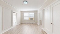 Located on the third floor at 4961 Laclede Ave in St. Louis's Central West End neighborhood, this well-appointed unit offers a thoughtfully organized layout across a single floor. The space is characterized by classic architectural detailing throughout, including elegant wainscoting and panel molding on the walls, crisp white trim, and light hardwood-style flooring that flows seamlessly from room to room.

The living room is bright and airy, benefiting from natural light through windows dressed with horizontal blinds, and features a traditional wall-unit radiator alongside a window air conditioning unit. The galley-style kitchen is efficiently designed with white shaker cabinetry extending to the ceiling, a white subway tile backsplash, light stone countertops, and stainless steel appliances including a gas range, dishwasher, and refrigerator. A combined dining area adjoins the kitchen, making the space practical for everyday living.

The bathroom stands out with decorative encaustic-style patterned floor tile in gray and white, a clean white subway-tiled tub and shower surround, and a window that brings in natural light. Built-in shelving adds functional storage. Four closets distributed throughout the unit provide ample storage. A connecting hallway ties the layout together, contributing to the unit's efficient and cohesive flow.