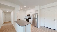 Located at 4001 E Jory St in Newberg, Oregon, this well-designed single-story home offers four bedrooms and two bathrooms within a thoughtfully organized floor plan. The open-concept living, dining, and kitchen area serves as the heart of the home, bathed in natural light from large windows and a glass balcony door that provides outdoor access. Light wood-style flooring runs throughout, complementing the clean, neutral palette of white walls and trim.

The kitchen is a standout feature, equipped with stainless steel appliances including a refrigerator, microwave, and electric range. White shaker-style cabinetry extends to the ceiling, offering generous storage, while a peninsula with a dark granite-style countertop provides additional workspace and casual dining space.

The four bedrooms are bright and well-proportioned, each featuring large windows with blinds that invite natural light and outdoor views of the surrounding Newberg landscape. The spacious primary bedroom includes its own access point, adding a layer of privacy. Three closets are distributed throughout the unit for ample storage.

Both bathrooms maintain the home's clean aesthetic with white cabinetry, dark countertops, large mirrors, and light wood flooring. A dedicated laundry area and hallway complete the efficient layout, making this home as functional as it is modern.