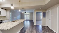 Located on Juniper Street NE in Atlanta, Georgia, this single-floor residence offers a thoughtfully designed layout with contemporary finishes throughout. The open-concept kitchen serves as a central hub, featuring granite countertops, white cabinetry, stainless steel appliances including a refrigerator, range, and microwave, and a peninsula with pendant lighting overhead. Wood-style flooring extends through the kitchen and main living areas, providing a cohesive, modern aesthetic.

The living area is bright and welcoming, highlighted by French doors with transom windows above that invite natural light and provide access to an outdoor balcony. Crown molding and ceiling fans add refined detail to the living spaces. Bedrooms are carpeted for comfort and include ceiling fans and windows with outdoor views of surrounding greenery. One bedroom also features French door access to a balcony, while a generously sized walk-in closet with wire shelving provides ample storage.

The bathrooms are finished with granite-topped vanities, white cabinetry, wood-style flooring, and tiled tub-shower combinations. The overall palette of neutral tones and gold-toned hardware creates a warm, cohesive ambiance throughout this well-appointed Atlanta residence.
