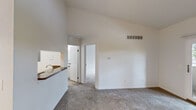 The Amsterdam is a thoughtfully designed 1-bedroom, 1-bathroom residence that makes efficient use of its single-floor layout. The living area is immediately impressive thanks to soaring vaulted ceilings that lend a sense of openness, complemented by neutral carpet flooring and crisp white walls. A pass-through counter connects the living space to the kitchen, which features white cabinetry with brushed nickel hardware, granite-style countertops, stainless steel appliances including a refrigerator and range, and light tile flooring. Adjacent to the kitchen, the dining area benefits from a decorative chandelier and direct access to the kitchen, creating a natural flow for entertaining. The bedroom is a comfortable retreat with vaulted ceilings, plush carpet, and a large window that brings in natural light and outdoor views. It includes a dedicated walk-in closet outfitted with wire shelving, offering generous storage. A second closet with bifold doors is also present in the dining area. The bathroom features a full tub/shower combination with a curtain rod, a toilet, and a vanity with a granite-style countertop, all finished with tile flooring. A hallway connects the key areas of the residence, completing this well-organized and functional floor plan.
