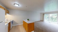 Located at 4611 SW Luradel St in Portland, Oregon, this one-bedroom, one-bathroom unit offers a well-organized and functional layout across a single floor. The open living area is finished with neutral-toned carpet and features a sliding glass door that leads to a balcony overlooking lush, tree-lined surroundings, bringing natural light and a sense of connection to the outdoors. The kitchen is equipped with warm-toned wooden cabinetry, white appliances including a refrigerator, dishwasher, electric range, and a peninsula island with a light countertop — providing both prep space and a natural division between the kitchen and living areas. Light wood-style flooring runs throughout the kitchen and bathroom, creating a clean contrast with the carpeted living and sleeping spaces. The bedroom is a comfortable size, featuring a window with greenery views, soft carpet, and convenient access to both a dedicated closet and the full bathroom. The bathroom includes a combined tub and shower enclosed by frosted sliding glass doors, warm wood cabinetry, and light flooring, maintaining the unit's consistent, practical aesthetic. Textured ceilings and neutral wall tones throughout give the space a cohesive, move-in-ready feel.