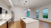 Located at 770 Neil Ave in Columbus, OH, this modern 2-bedroom, 2-bathroom unit offers a thoughtfully designed single-floor layout with clean contemporary finishes throughout. The kitchen is a standout feature, boasting a large waterfall-edge island with an undermount sink, stainless steel appliances including a range, microwave, and French door refrigerator, warm wood-toned lower cabinetry paired with light upper cabinets, white quartz countertops, and stylish pendant lighting overhead. Light hardwood flooring runs throughout the kitchen and living areas, adding warmth to the bright, open space. Both bedrooms are carpeted and filled with natural light from large windows. The spacious primary bedroom features multiple windows offering treetop and city views, while the second bedroom overlooks the building's modern exterior courtyard. A dedicated closet provides ample storage. Both bathrooms are finished in a consistent modern style, featuring floating wood-grain vanities with white quartz countertops, round wood-framed mirrors, and clean white tile. One bathroom includes a shower-tub combination. A private balcony with metal railings offers views of the surrounding contemporary multi-story building complex. The unit's crisp white walls and minimalist design create a cohesive, move-in-ready living environment.