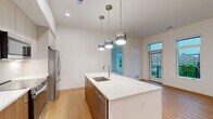 Located at 770 Neil Ave in Columbus, OH, this modern 2-bedroom, 2-bathroom unit offers a thoughtfully designed single-floor layout with clean contemporary finishes throughout. The kitchen is a standout feature, boasting a large waterfall-edge island with an undermount sink, stainless steel appliances including a range, microwave, and French door refrigerator, warm wood-toned lower cabinetry paired with light upper cabinets, white quartz countertops, and stylish pendant lighting overhead. Light hardwood flooring runs throughout the kitchen and living areas, adding warmth to the bright, open space. Both bedrooms are carpeted and filled with natural light from large windows. The spacious primary bedroom features multiple windows offering treetop and city views, while the second bedroom overlooks the building's modern exterior courtyard. A dedicated closet provides ample storage. Both bathrooms are finished in a consistent modern style, featuring floating wood-grain vanities with white quartz countertops, round wood-framed mirrors, and clean white tile. One bathroom includes a shower-tub combination. A private balcony with metal railings offers views of the surrounding contemporary multi-story building complex. The unit's crisp white walls and minimalist design create a cohesive, move-in-ready living environment.