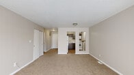 This single-floor residence offers a practical and comfortable layout designed for everyday living. The open living area is generously sized, featuring warm neutral-toned carpeting, light-colored walls, and a large sliding glass door that fills the room with natural light and provides views of the surrounding outdoor greenery. A sliding-door closet adds convenient storage directly off the main living space.

The kitchen is accessible via an open pass-through from the living area and is outfitted with dark gray cabinetry, light countertops, a stainless steel sink, and wood-look flooring. White appliances, including a refrigerator and range, round out the functional setup. A separate utility area with additional appliances is tucked just beyond the kitchen.

The bedrooms continue the warm, neutral aesthetic with plush carpeting and soft gray walls. One bedroom features a dedicated walk-in closet equipped with wire shelving systems, offering excellent organization and storage capacity. A window in the secondary bedroom allows for natural light.

The bathroom is clean and bright, featuring a full-size soaking tub with a tiled surround, chrome fixtures, and wood-look flooring. The overall design of this residence prioritizes functionality and comfort, with a cohesive neutral palette throughout.