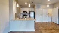 This single-floor residence offers a thoughtfully designed layout that balances open communal spaces with comfortable private areas. The living room is bright and welcoming, featuring warm wood-look luxury vinyl plank flooring, neutral-toned walls, a ceiling fan with light fixture, and a window with exterior views that fill the room with natural light. A door provides direct access to the outdoors, enhancing the sense of openness.

The kitchen is a standout feature, centered around a granite-topped island with an integrated sink and pendant lighting overhead. White shaker cabinetry lines the walls, complemented by stainless steel appliances including a refrigerator, range, microwave, and dishwasher. The same wood-look flooring continues seamlessly throughout this space, tying the kitchen and living areas together.

The bedrooms are carpeted for comfort, each offering neutral walls, natural light through blinds-fitted windows, and ceiling fans. Closets with built-in shelving and hanging rods provide ample storage. The bathroom is finished with white cabinetry topped with granite countertops, wood-look flooring, and a shower and tub combination enclosed by a curtain. Clean lines and a neutral palette are consistent throughout, creating a cohesive and functional living environment.