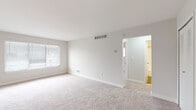 This single-floor residence offers a clean, neutral design throughout, making it a versatile and move-in-ready space. The layout, visible from the floor plan, flows logically between living, sleeping, kitchen, and bathroom areas.

The living area is generously sized, featuring soft wall-to-wall carpeting in a warm beige tone and multiple windows dressed with white horizontal blinds. Natural light fills the room, highlighting the crisp white walls and clean baseboard trim. A transition to wood-look flooring marks the entry into the kitchen and connecting spaces.

The kitchen is well-appointed with a galley-style layout, featuring stainless steel appliances — including a refrigerator, range, microwave, and dishwasher. White upper cabinetry with modern hardware contrasts with warm wood-toned lower cabinets, complemented by white quartz-style countertops and a classic white subway tile backsplash. Wood-look flooring runs throughout, and a louvered closet door at the end provides additional storage.

The bedroom areas continue the carpeted flooring and bright, neutral aesthetic, each with windows allowing natural light. The bathroom includes a full tub-shower combination with white tile surround, gold-toned fixtures, and wood-look flooring, maintaining a cohesive and refreshed look throughout the unit.