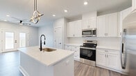 Located in South Lebanon, Ohio, this thoughtfully designed single-floor residence offers a generous, open-concept layout that balances modern aesthetics with everyday functionality. The combined kitchen and living area serves as the heart of the home, anchored by a large quartz-topped island with an undermount sink and a striking sculptural pendant light. White shaker cabinetry lines the kitchen walls alongside stainless steel appliances, including a range, over-the-range microwave, and a French-door refrigerator. A dedicated pantry provides additional storage. Warm wood-look flooring flows throughout the entire space, complementing the soft gray walls and crisp white trim. The living room is bright and spacious, featuring recessed lighting, a ceiling fan, and French doors that open onto a private balcony. From the balcony, expansive views of rolling green fields and open Ohio countryside create a serene outdoor retreat. The bedroom is well-proportioned, benefiting from its own ceiling fan and direct access to a walk-in closet. The full bathroom is finished with a white shaker vanity, quartz countertop, matte black hardware, and a tub-shower combination. A utility room and additional closet space round out this clean, move-in-ready residence.