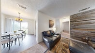 This thoughtfully designed 1-bedroom, 1-bathroom unit offers a comfortable and functional layout across a single floor. The living room serves as the centerpiece of the space, highlighted by a striking reclaimed wood plank accent wall that adds a rustic, textural contrast to the otherwise clean, neutral walls and textured ceiling. Carpet flooring adds warmth to this area, which flows naturally toward the dining room.

The dining area features hard-surface flooring and is bathed in natural light from a sliding glass door that opens to a private balcony, offering pleasant outdoor views of surrounding greenery. The galley-style kitchen is efficiently organized with white cabinetry, dark countertops, and black appliances including a range, dishwasher, and refrigerator, all set above rich hardwood-style flooring.

The spacious primary bedroom includes plush carpet, a ceiling fan, and access to a dedicated walk-in closet with built-in shelving for ample storage. The full bathroom features a wide vanity with dark countertops, white cabinetry, a large mirror, and hardwood-style flooring, providing a clean and functional space. A hallway connects the rooms cohesively, completing this compact yet well-equipped single-floor residence.