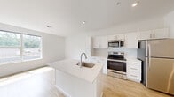 This single-floor residence features a clean, contemporary design throughout, with a bright white palette and quality finishes that create a cohesive, modern aesthetic. Light-toned hardwood-style flooring runs through the main living and kitchen areas, while plush carpeting adds comfort to the bedrooms.

The open-concept kitchen is a standout feature, anchored by a large center island with a white quartz countertop and an undermount sink. White shaker-style cabinetry lines the walls, complemented by a geometric tile backsplash and a full suite of stainless steel appliances, including a range, microwave, and refrigerator. Recessed lighting and a large window flood the space with natural light.

The living area is generously sized, featuring a sliding glass door that opens to a private balcony overlooking greenery and the surrounding neighborhood. Additional windows bring in ample daylight and outdoor views.

The bedrooms are well-proportioned, carpeted, and include double-door closets. Two bathrooms serve the unit — one featuring a tub-shower combination and hardwood-style flooring, and the other a clean vanity with quartz countertop. A central hallway with panel-style doors connects all areas of the home efficiently.