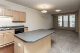 This single-floor residence is organized around a functional, open-concept layout that seamlessly connects the kitchen to the living area. The kitchen is well-appointed with light maple cabinetry offering generous upper and lower storage, dark laminate countertops, a double basin sink, and a full suite of black appliances including a refrigerator, range, built-in microwave, and dishwasher. Rich hardwood-style flooring anchors the kitchen, while a peninsula island provides additional counter space and serves as a natural dividing point between the kitchen and the adjoining living area.

The living area transitions to plush wall-to-wall carpeting and receives natural light through windows that frame exterior building views. Flush-mount and pendant light fixtures provide consistent overhead illumination throughout. The bedrooms are carpeted and modestly sized, each featuring windows and proximity to closet access, maintaining a calm and functional atmosphere.

The bathrooms are finished with tile flooring in an earthy tone, light wood vanities with integrated sinks, large mirrors, and accessibility-oriented grab bars. One bathroom includes a full soaking tub and shower combination. Textured ceilings and neutral warm tones are consistent throughout, giving the space a cohesive and understated aesthetic.