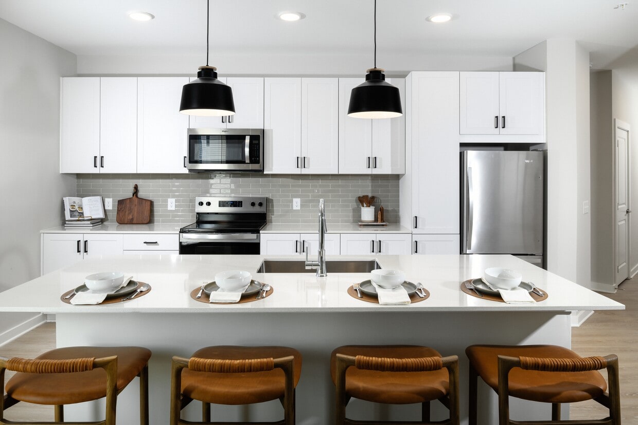 Cocina con gabinetes blancos tipo shaker, encimeras de cuarzo blanco, protector contra salpicaduras de azulejos grises y electrodomésticos de acero inoxidable. - Avalon Lake Norman