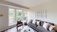 This single-floor residence is thoughtfully designed with a cohesive contemporary aesthetic carried throughout. The living room is bright and welcoming, anchored by a large picture window that frames lush tree views and fills the space with natural light. Neutral warm-beige walls, wood-look flooring, and curated wall art contribute to a calm, polished atmosphere.

The kitchen is a standout feature, showcasing white shaker-style cabinetry, dark granite countertops, and a full suite of stainless steel appliances including a gas range, over-the-range microwave, and French door refrigerator. A two-toned island with seating provides both prep space and casual dining. Pendant lighting adds a refined finishing touch.

The open layout allows the kitchen and living areas to flow naturally into one another, enhancing the sense of space. A dedicated in-unit laundry area with a full-size washer and dryer offers everyday convenience, positioned adjacent to the bedroom, which receives natural light and features access to an outdoor balcony.

The bathroom is finished with dark-tiled flooring, a gray vanity with white quartz countertop, brushed nickel fixtures, and a tub-shower combination, delivering a clean, modern feel.